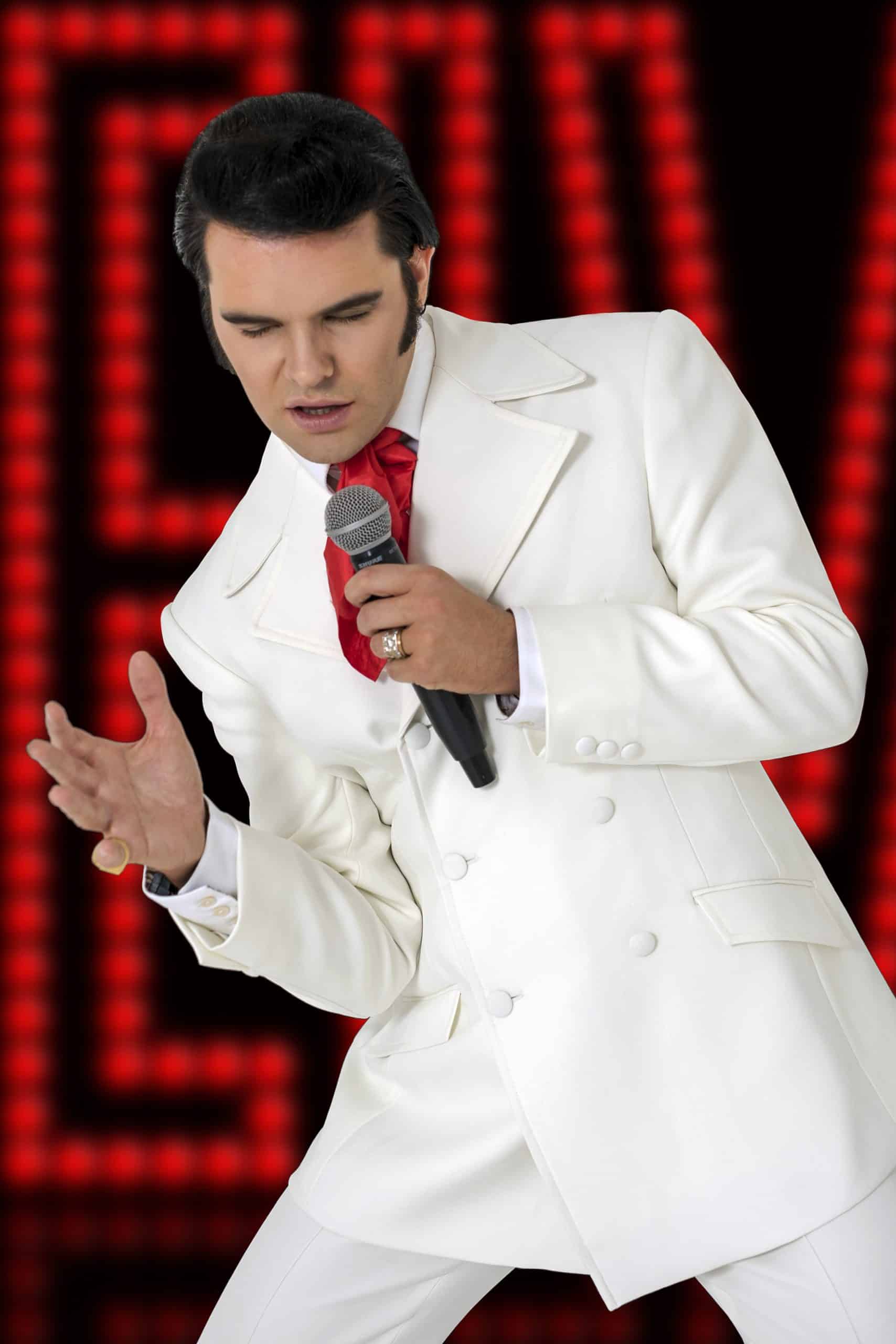 Elvis impersonator JD King dressed in white in front of a red neon sign